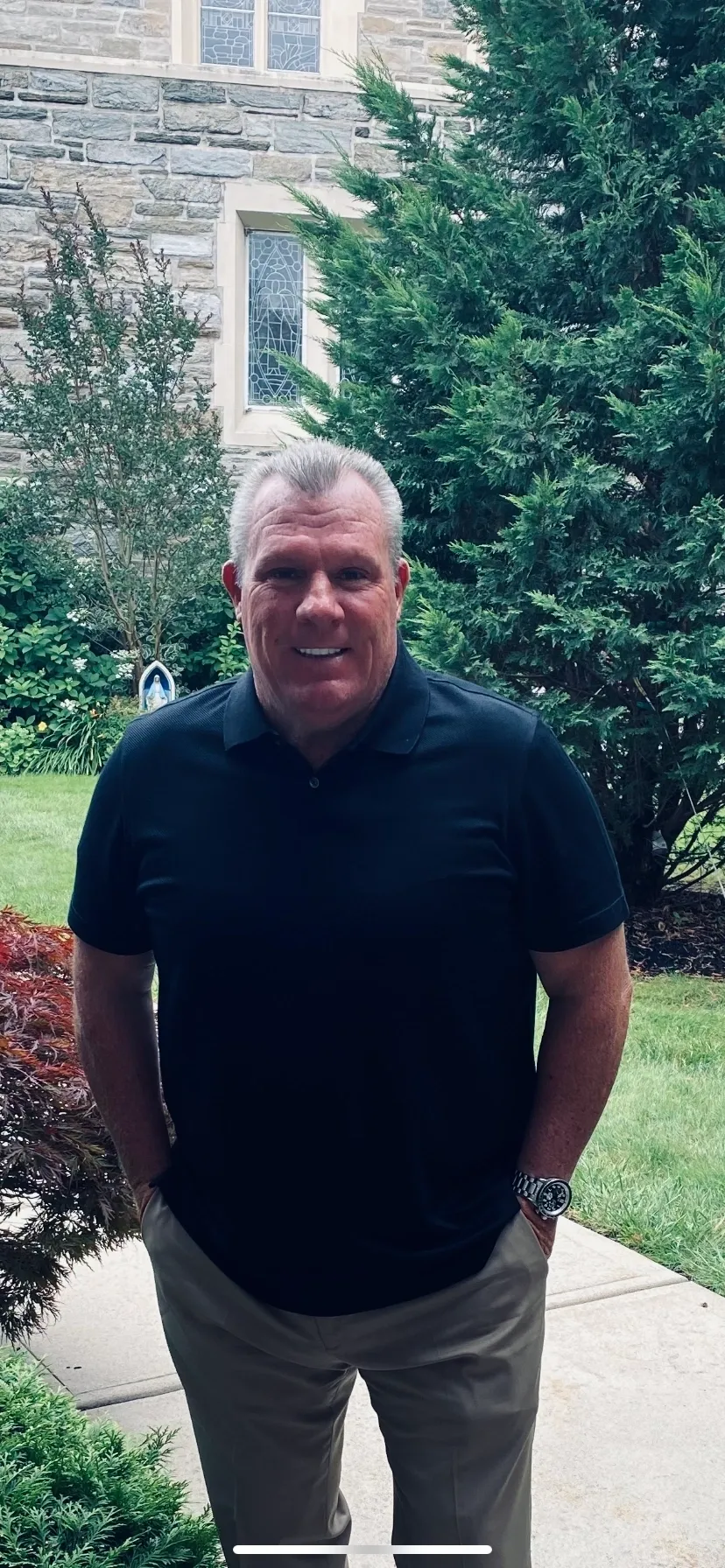 Smiling man in black polo near stone church