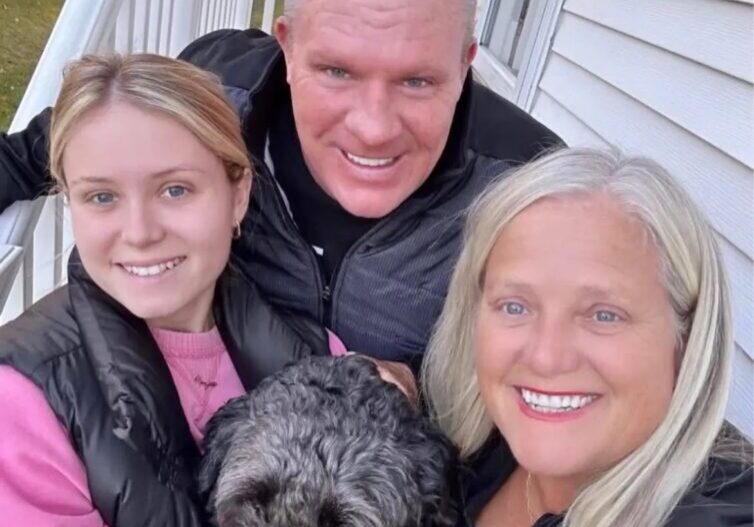 Family smiling with dog on porch steps.