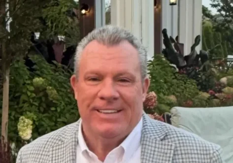 Smiling man in checkered jacket outside building.