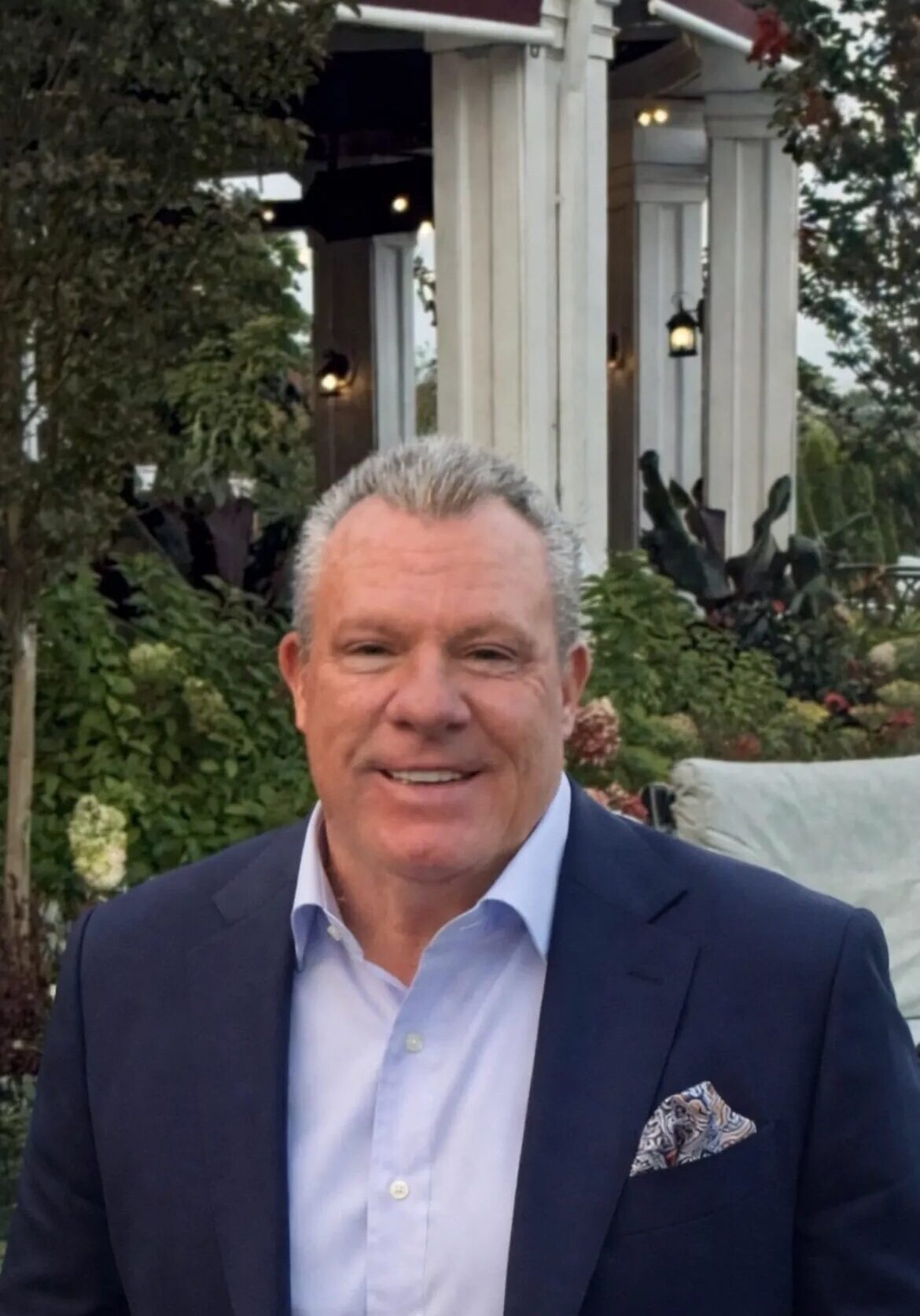Smiling man in navy suit at garden pavilion