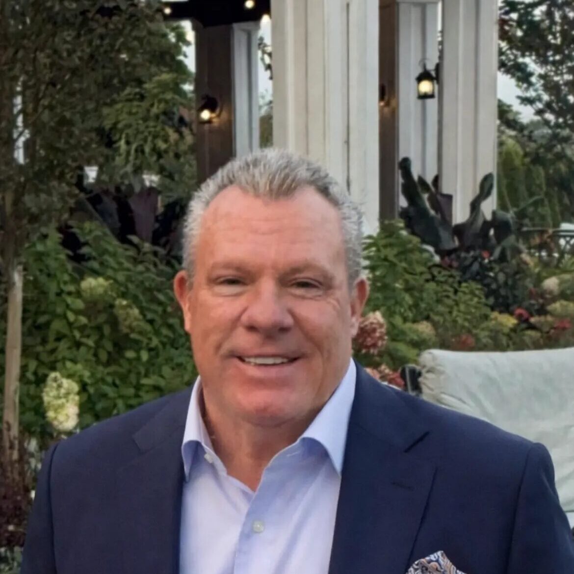 Smiling man in navy suit at garden pavilion